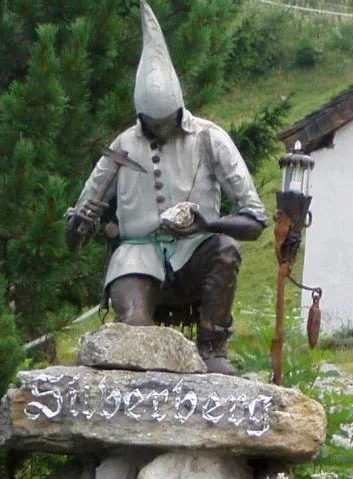 Knieender Bergknappe aus getriebenem Bronzeblech mit spitzer Mütze, davor ein Schild mit der Aufschrift Silberberg